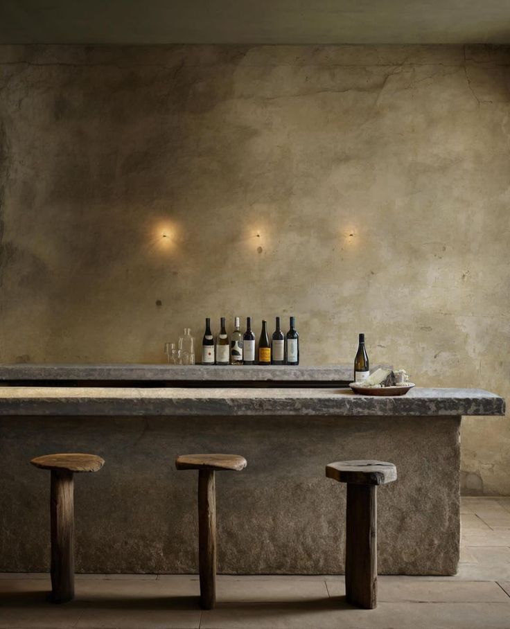 an empty bar with stools and bottles on the counter in front of concrete walls