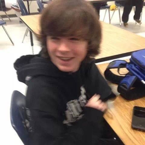 a young man sitting at a table with his arms crossed and smiling for the camera