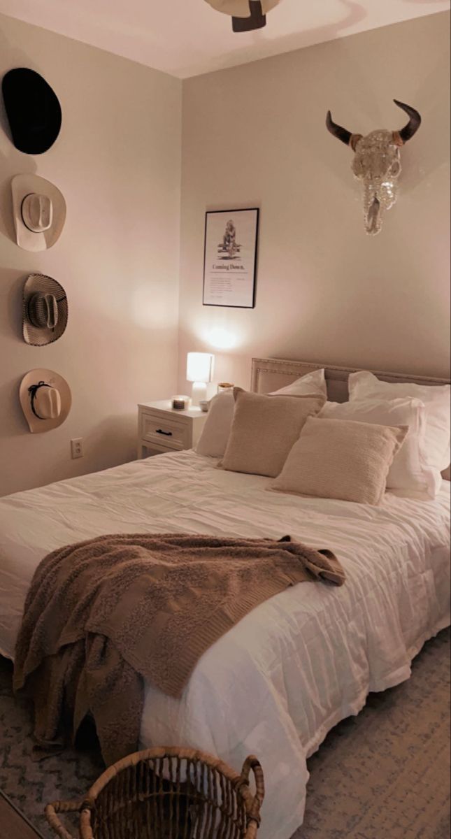 a bed with white sheets and pillows in a bedroom next to a cow head mounted on the wall