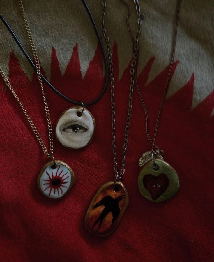 four different necklaces on a red and white cloth with an image of a person's eye