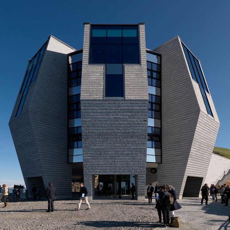 people are walking around in front of a building with two triangular shaped windows on it