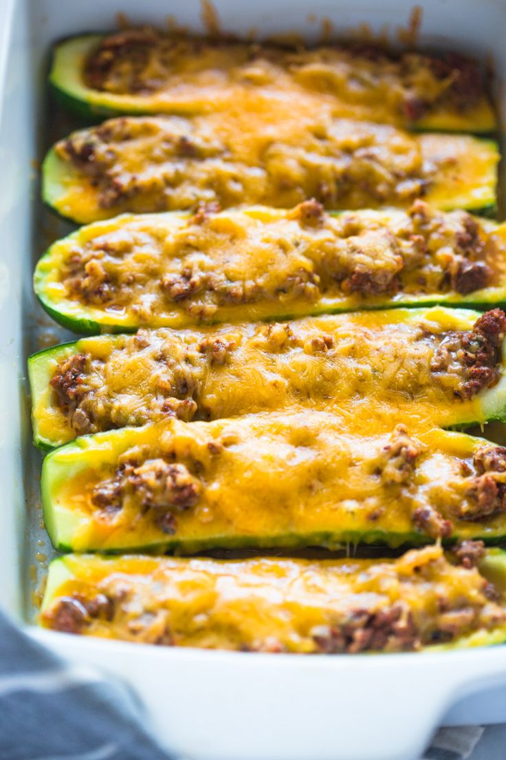 stuffed zucchini boats in a white casserole dish with meat and cheese