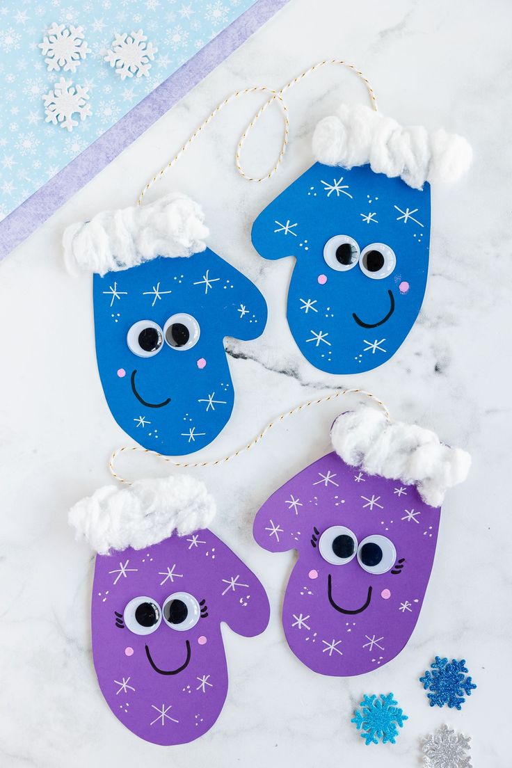 three purple and blue paper mittens with snowflakes hanging from the side on a marble surface