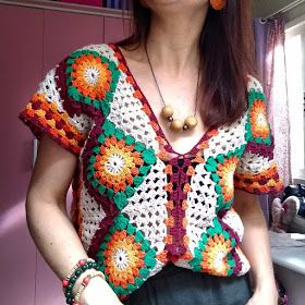 a woman standing in front of a window wearing a crocheted top and earrings