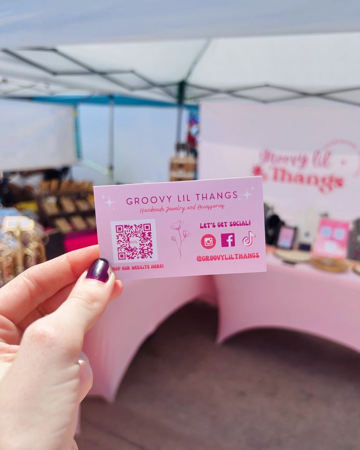 a person holding up a pink business card in front of a booth at a market