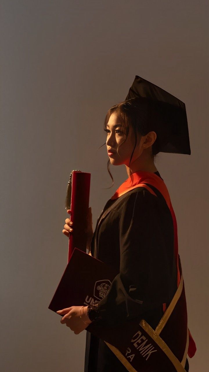 a woman wearing a graduation gown and holding a red book in one hand while standing against a white background