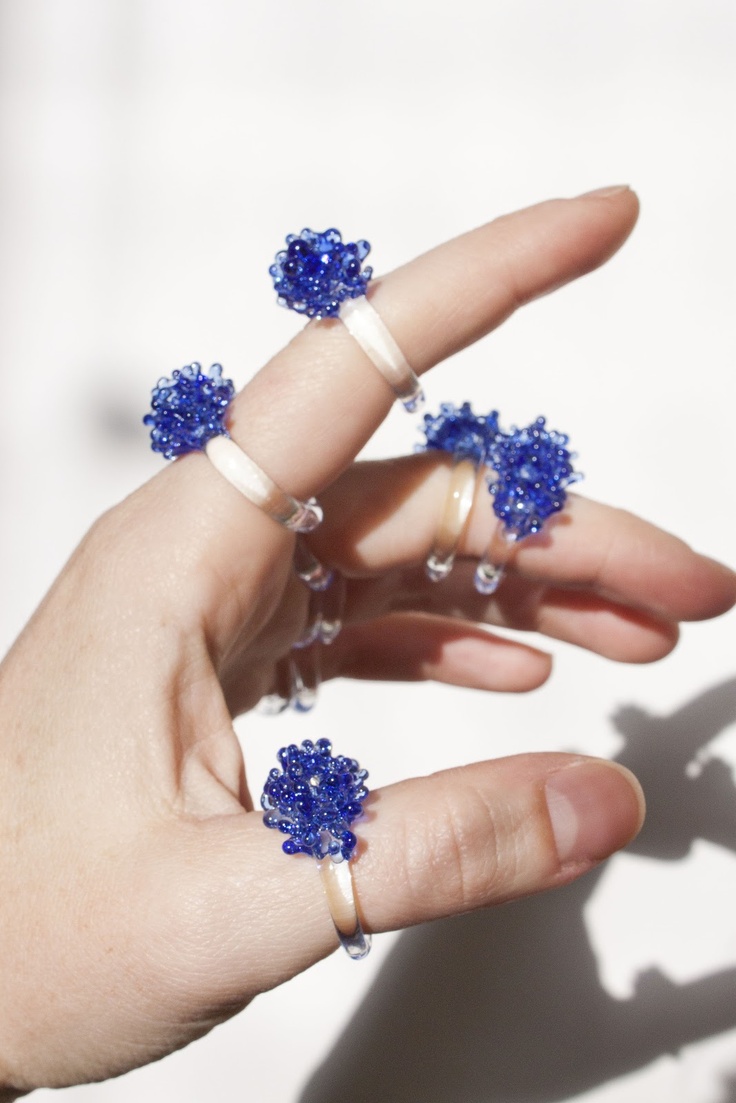 a person's hand is holding three rings with blue beads on them and two fingers