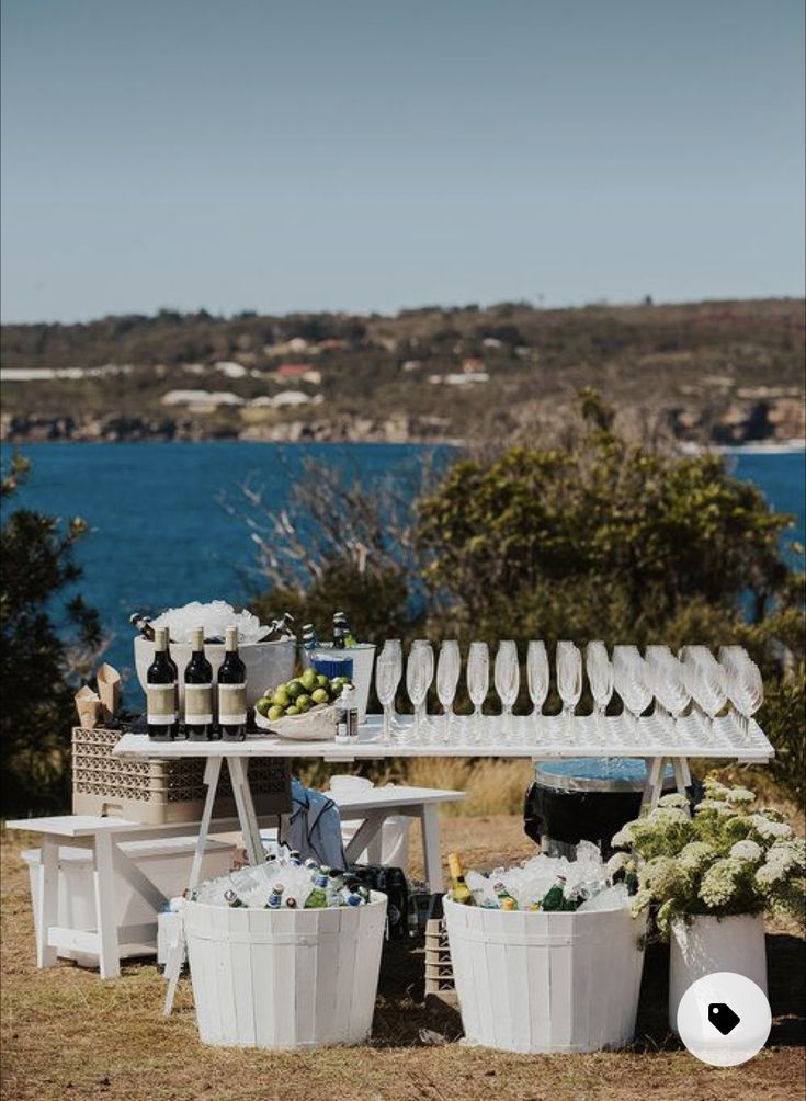 an outdoor table set up with wine glasses and plates on it, next to the ocean