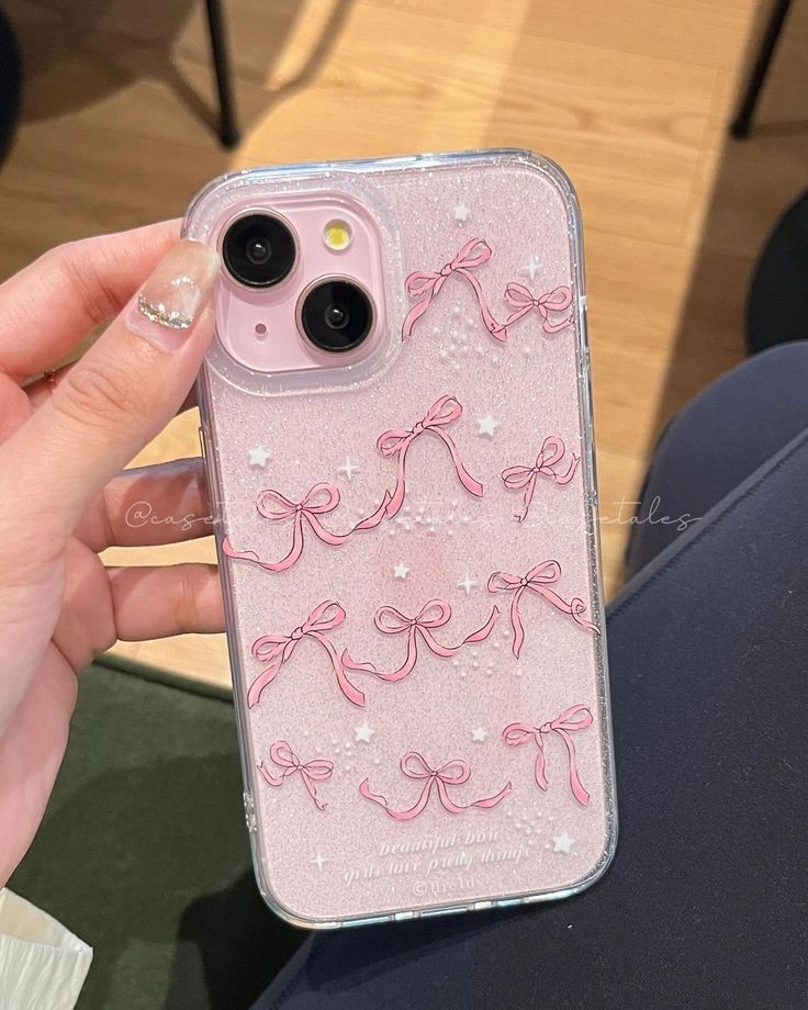 a person holding up a pink iphone case with bows and glitters on the back