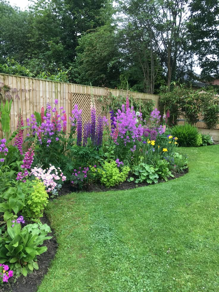 a garden filled with lots of flowers next to a wooden fence and green grass covered ground