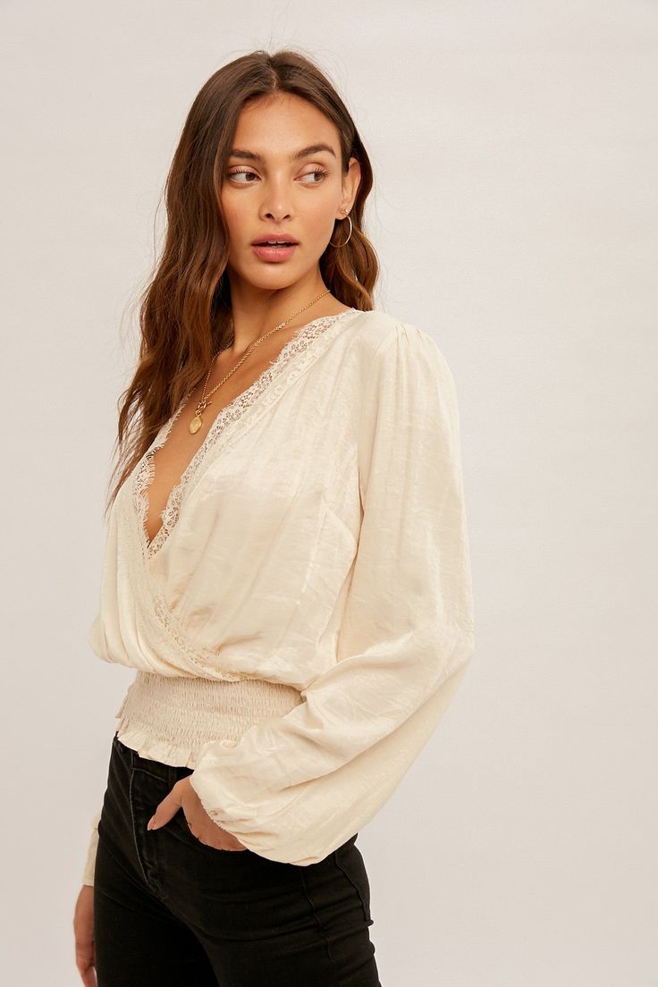 This Amir Blouse is ready to make some serious fashion waves! Crafted from a blend of rayon and polyester, the surplice lace-trimmed smock waist blouse is sure to add a classy and luxe touch to any outfit. Give your wardrobe an upgrade with this must-have piece! Feminine V-neck Tops With Lace Sleeves, Fitted V-neck Top With Elastic Waistband, V-neck Blouse With Lace Trim For Brunch, Feminine V-neck Lace Top For Day Out, V-neck Lace Top For Brunch, Elegant V-neck Lace Top For Fall, Chic Blouse With Smocked Back For Brunch, Long Sleeve Tops With Elastic Waistband For Day Out, Elegant V-neck Lace Top For Brunch