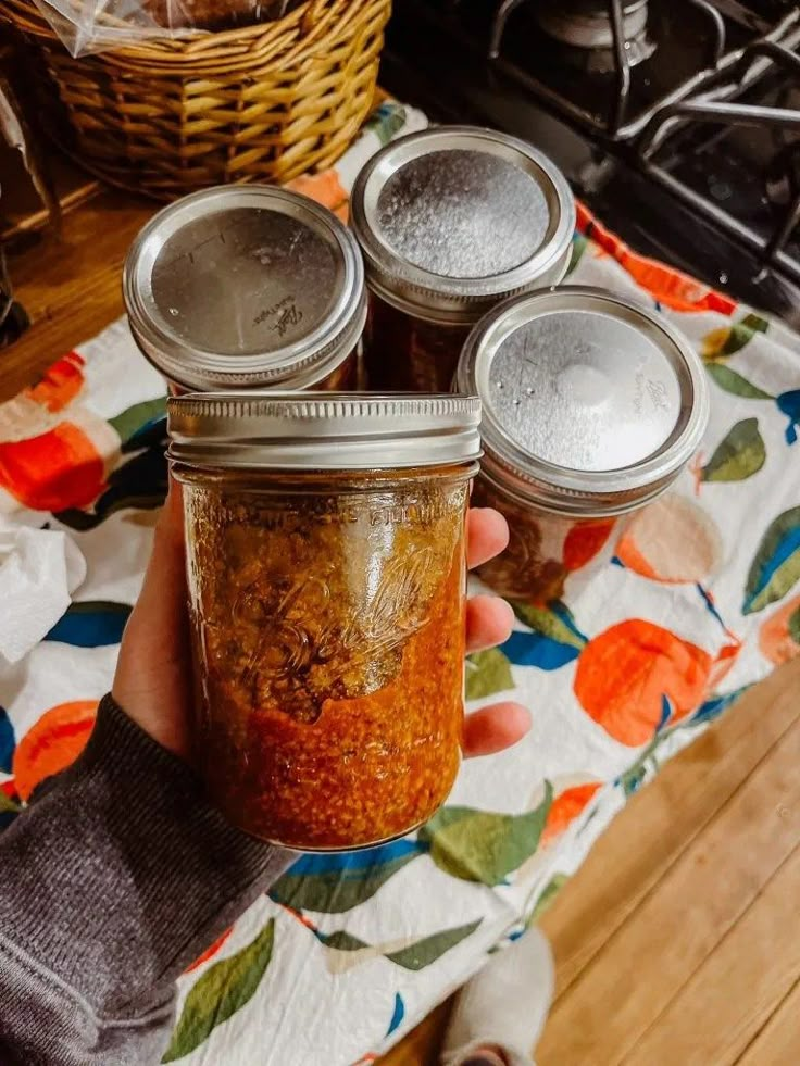 three jars of food sitting on top of a table next to a person's hand