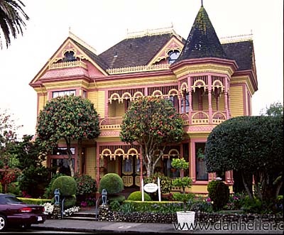 a pink and yellow victorian style house in the middle of a street with cars parked outside