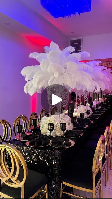 a table set up with black and gold chairs, white centerpieces and an ostrich feather centerpiece