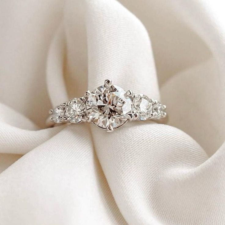 a diamond ring sitting on top of a white satin fabric with the center stone surrounded by smaller stones