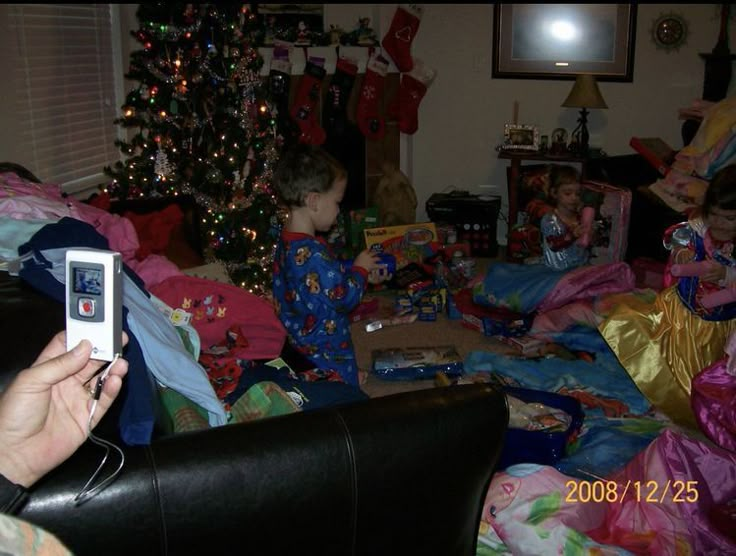 a woman taking a photo of two children in pajamas with christmas presents on the floor