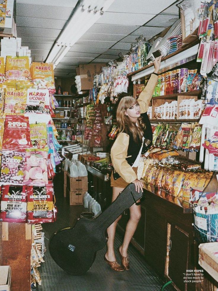 a woman standing in front of a store filled with food and drinks, reaching up to grab something out of the bag