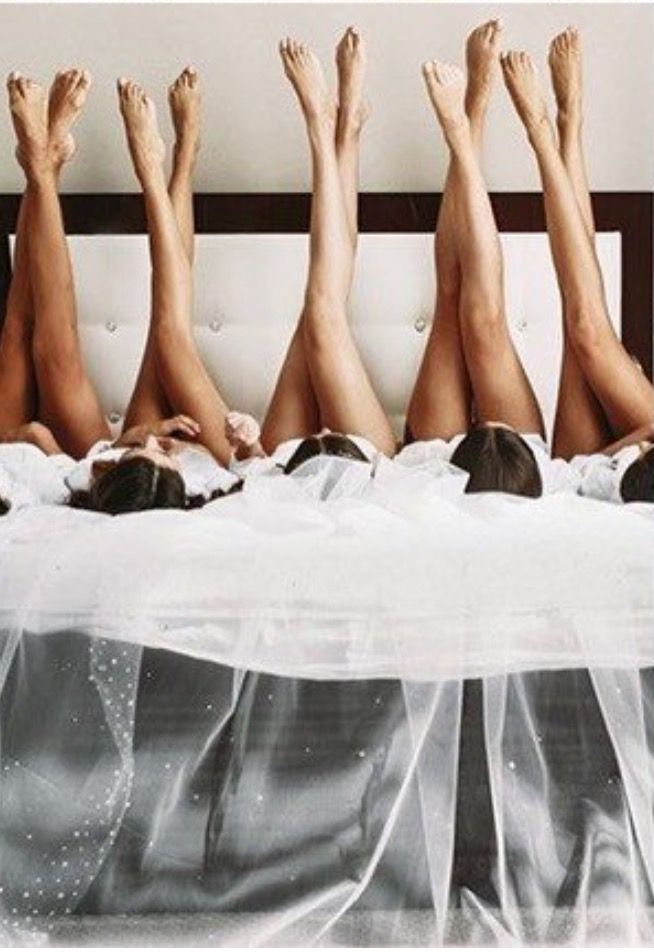 four women laying on top of a bed with white sheets and veils covering them