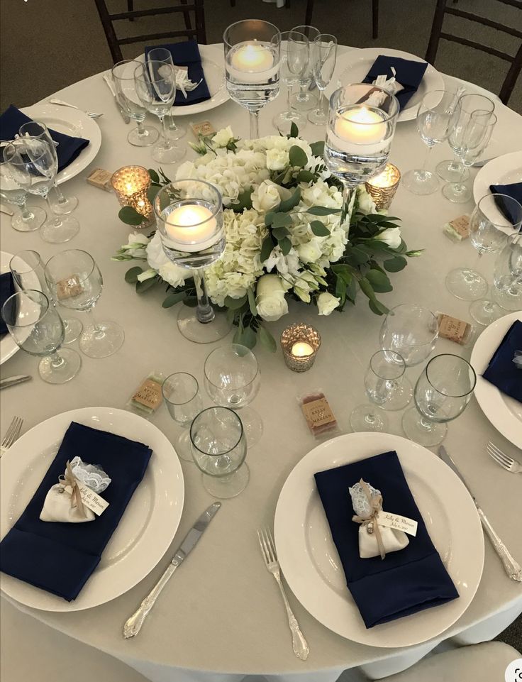 the table is set with white flowers and blue napkins, silverware and candles