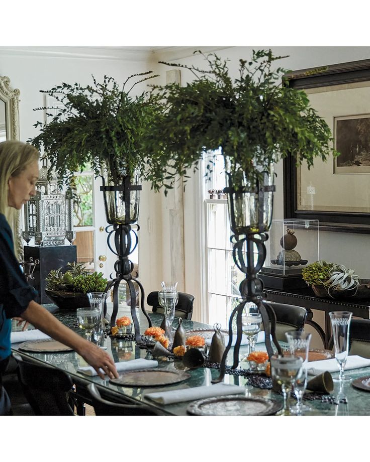 a woman standing in front of a dining room table set with place settings and flowers