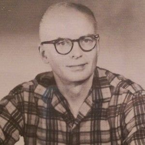 an old black and white photo of a man with glasses looking at the camera while wearing a plaid shirt