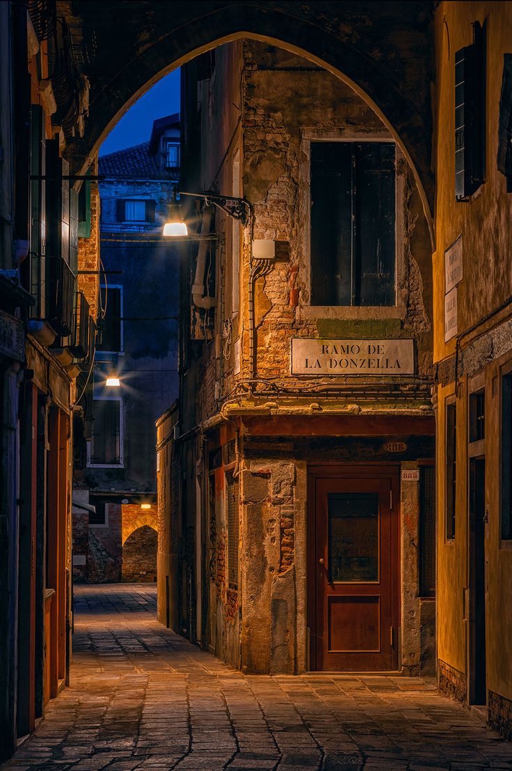 an alleyway with stone buildings and arched doorways at night, lit by street lights