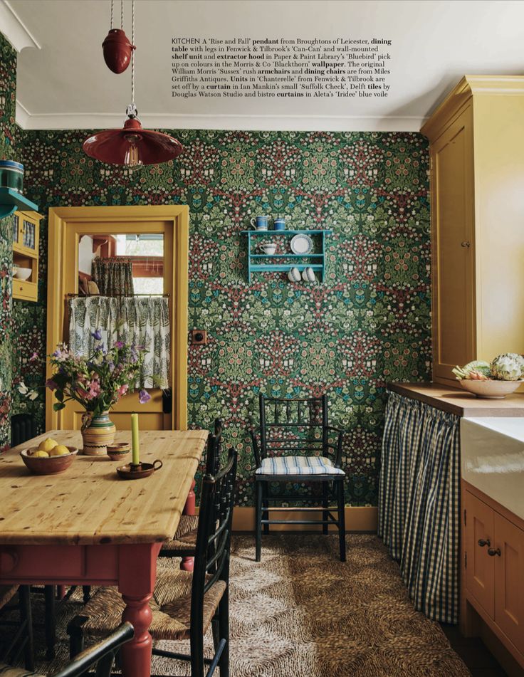 an old fashioned kitchen with floral wallpaper and wooden table in the center, along with two chairs