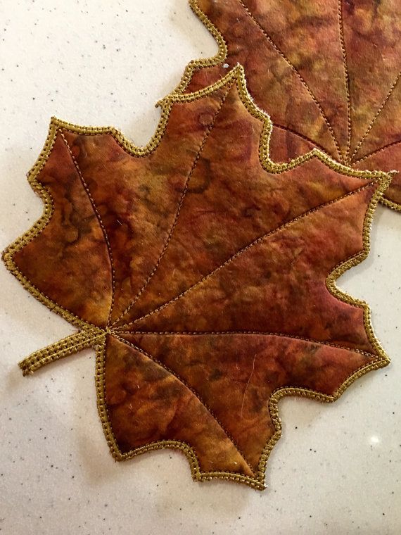 three autumn leaves on a white surface with gold stitching and sequins in the middle