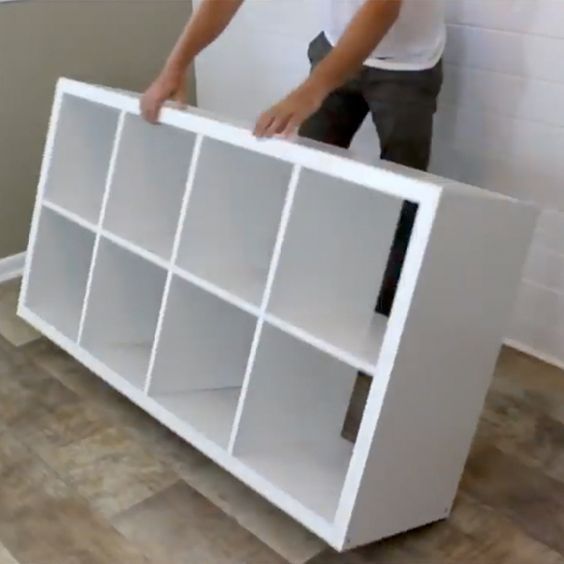 a man standing next to a white bookcase on top of a hard wood floor