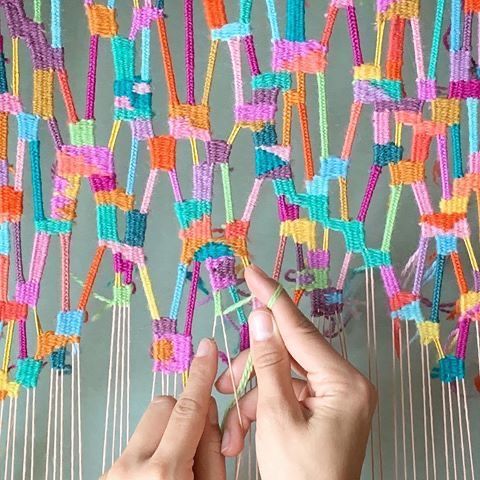 two hands are working on an art project made out of string and colorful yarns