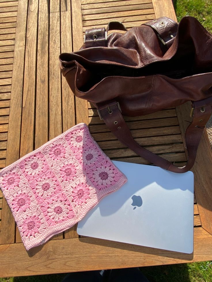 an apple laptop computer sitting on top of a wooden table next to a pink crocheted blanket