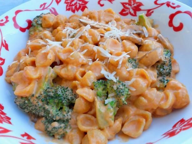 a pasta dish with broccoli and cheese in a red and white bowl on a table