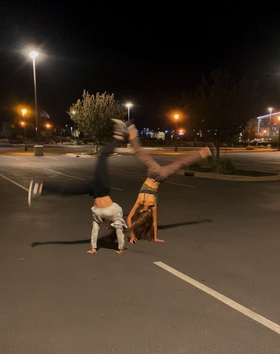 two people doing handstands in the middle of a parking lot at night time