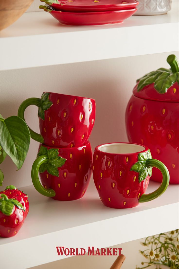 red ceramic strawberry mugs with green handles and strawberries on them, sitting on white shelves