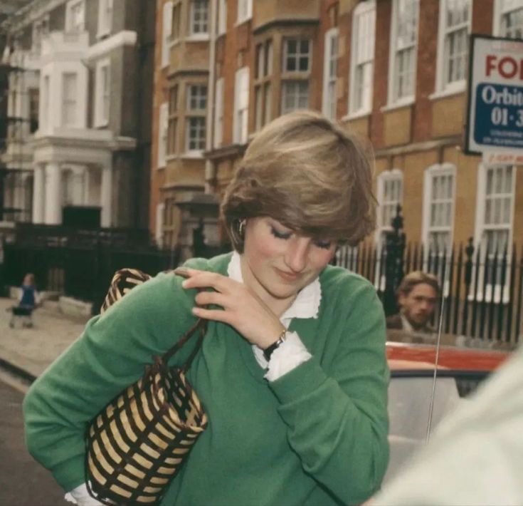 a woman is walking down the street with her hand on her shoulder and looking at her cell phone