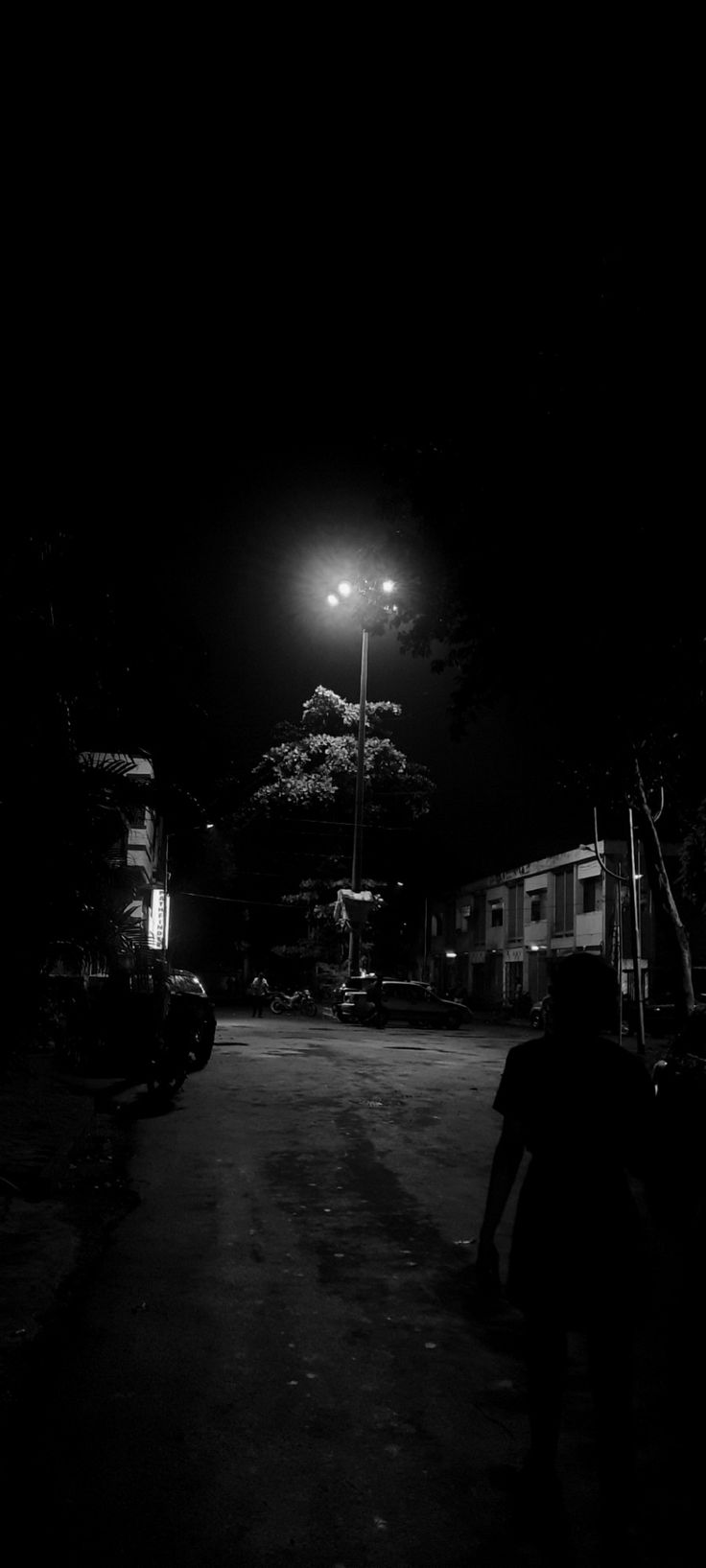 a person walking down a dark street at night with a light on in the background