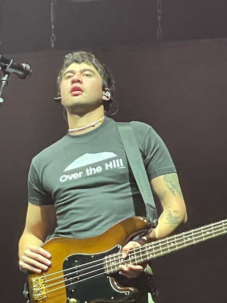 a man holding a bass guitar while standing next to a microphone and mic on stage