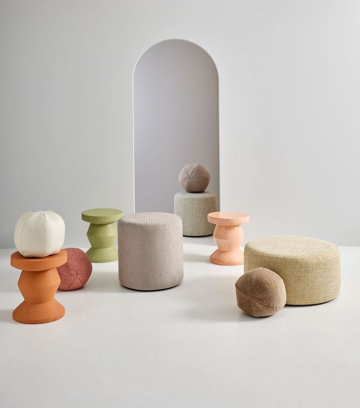 several different colored stools sitting in front of a white wall with a mirror behind them