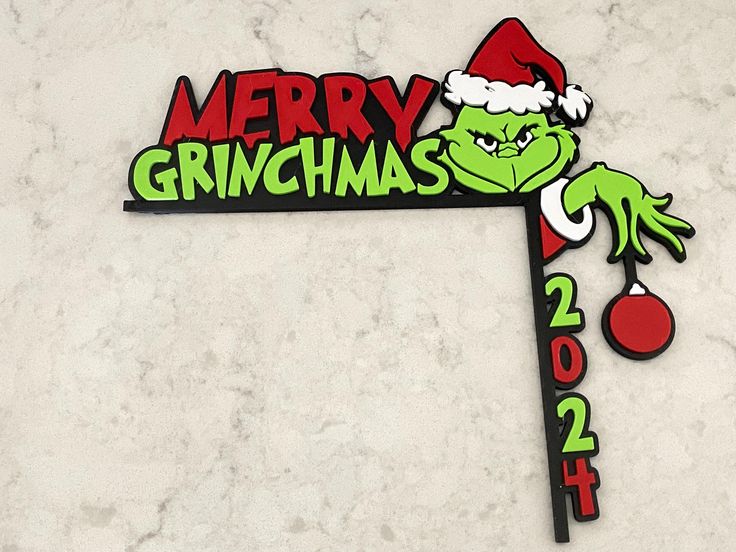 a christmas sign with the grinch on it's side and santa hat hanging from the top