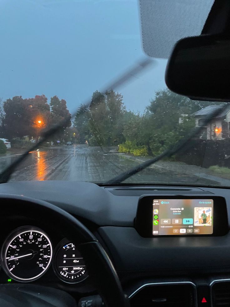 the dashboard of a car on a rainy day with rain and street lights in the distance