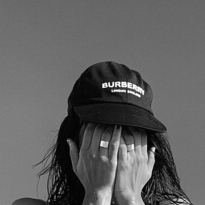 a woman covers her face with her hands while wearing a burber hat in black and white