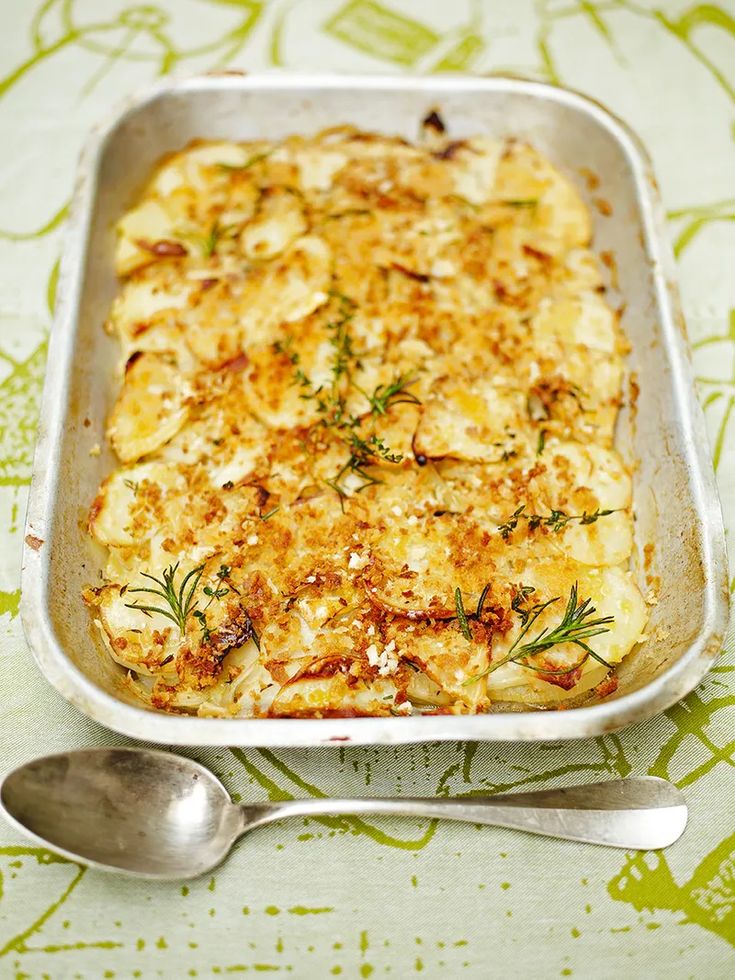 a casserole dish with cheese and herbs in it, next to a spoon