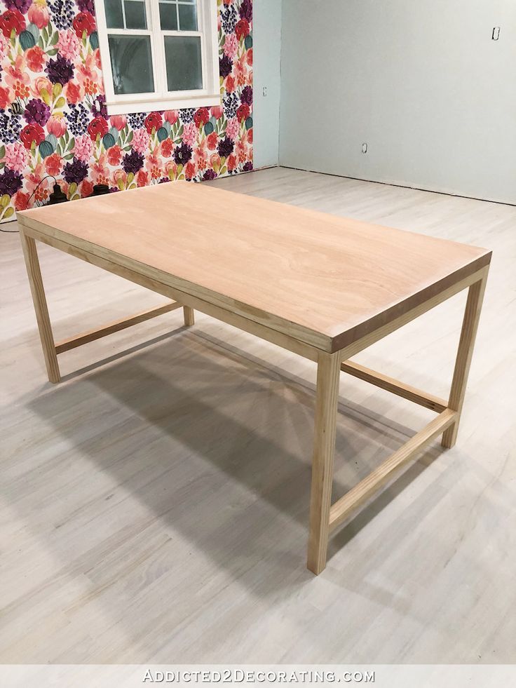 a wooden table sitting on top of a hard wood floor next to a wall covered in flowers