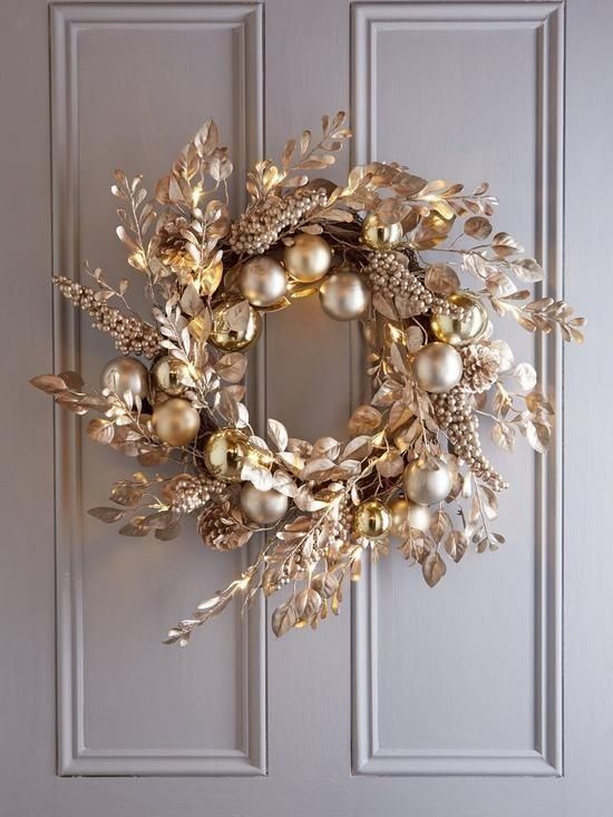 a wreath is hanging on the door with gold ornaments and greenery in front of it