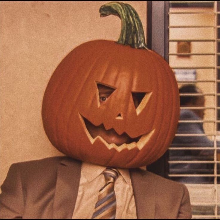 a man wearing a suit and tie with a pumpkin on his head in front of a window