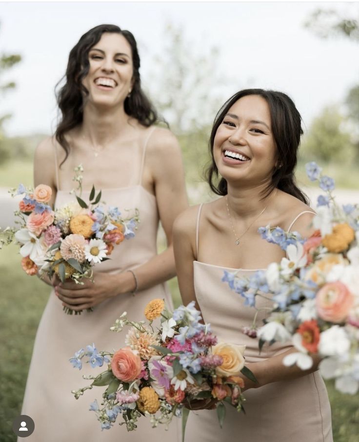 two beautiful women standing next to each other with bouquets in their hands and smiling at the camera