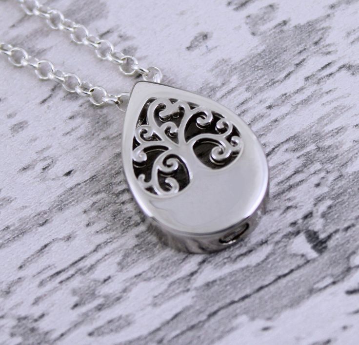 a silver necklace with a tree design on the front and back of it, sitting on a wooden surface