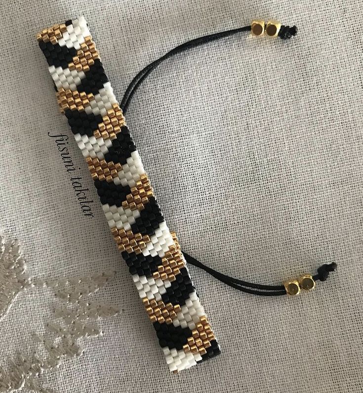 a black, white and gold beaded bracelet laying on top of a piece of fabric