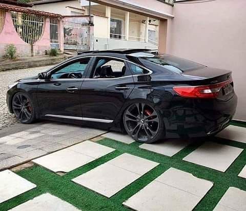 a black car parked in front of a pink building with green grass on the ground