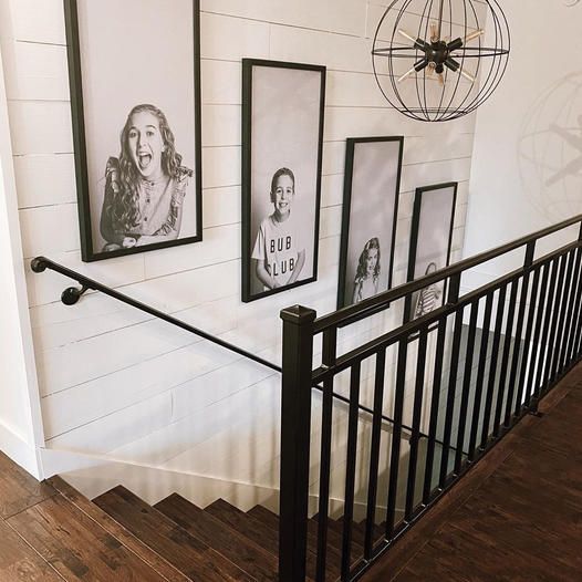 a stair case with pictures hanging on the wall next to it and an iron handrail